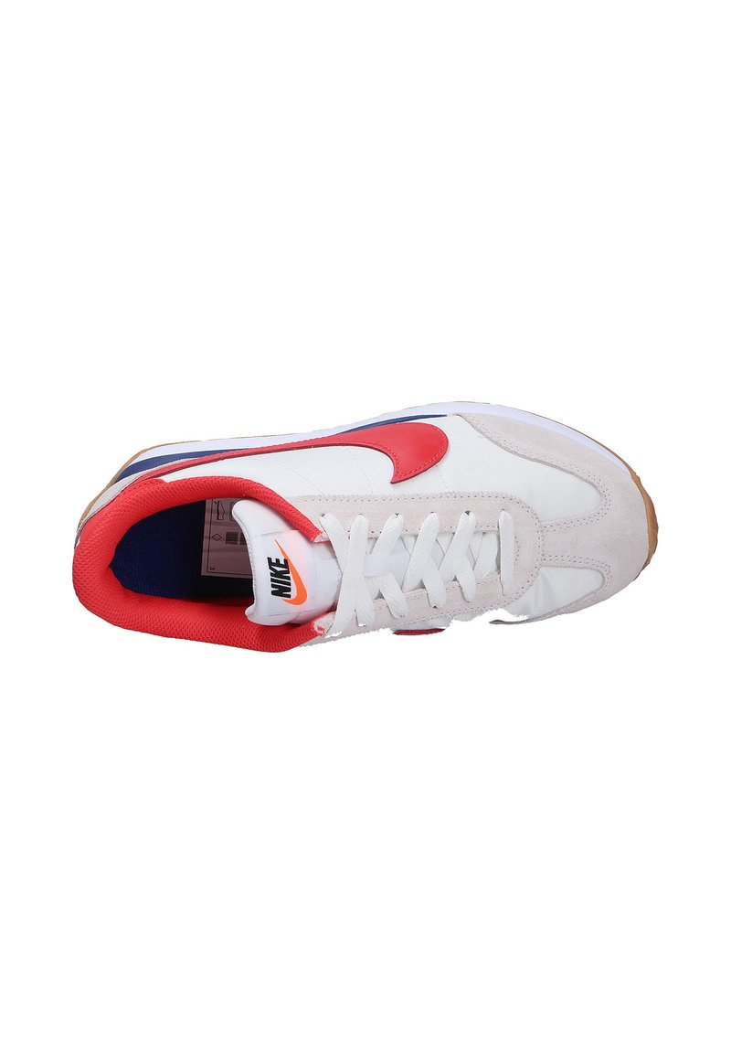 Zapatilla deportiva blanca con acentos rojos y azules, que cuenta con una parte superior de ante y tela, suela de goma y un logo prominente en la lengüeta y en el lateral.