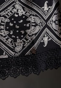 Schwarzer Stoff mit weißem Paisleymuster und Spitzenbesatz am unteren Rand. Verfügt über filigrane Muster und ein kleines metallic Akzent.