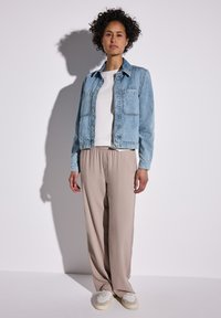 Chaqueta de mezclilla azul claro con dos bolsillos en el pecho, llevada sobre una camisa blanca, combinada con pantalones beige de pierna ancha y zapatillas crema.