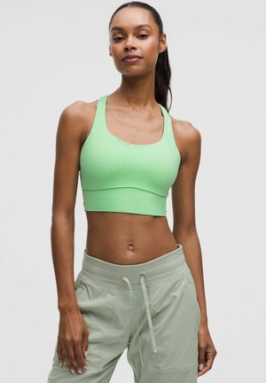 Reggiseno sportivo verde chiaro con design aderente, spalline larghe e texture liscia. Abbinato a pantaloni jogger verde chiaro con tasche.