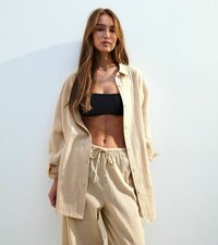 Beige knäppt skjorta över en svart crop top, tillsammans med ljusbeiga byxor med dragsko. Slät textur, avslappnad passform, minimalistisk design.