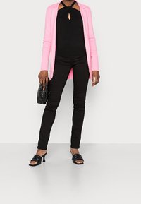 Blazer rosa, top halter nero con aperture, jeans skinny neri e sandali neri con tacco. Materiali texture, design elegante.