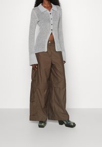 Cardigan open lavorato a maglia grigio chiaro con colletto e bottoni abbinato a pantaloni cargo marroni larghi. L'outfit presenta gambe ampie e un tessuto testurizzato.