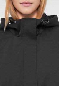 Μαύρο μπουφάν με κουκούλα, με λεία, ματ επιφάνεια, ρυθμιζόμενο κορδόνι στον γιακά και μινιμαλιστικό σχέδιο χωρίς μοτίβα.