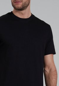 T-shirt nero a maniche corte realizzato in morbido tessuto, con un design classico a girocollo e una vestibilità aderente. Texture liscia senza motivi visibili.