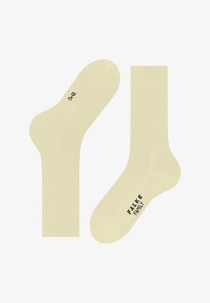 Jasnożółte skarpetki za kostkę wykonane z miękkiego materiału. Charakteryzują się gładką fakturą, standardowym kształtem oraz czarnym napisem "FALKE FAMILY".