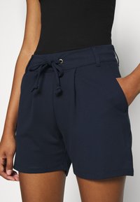 Shorts bleu marine en tissu doux ; dotés d'une taille élastique avec cordon de serrage, deux poches latérales, et une coupe décontractée avec un design minimaliste.