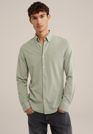 Camisa de botonadura verde claro con cuello, mangas largas y un sutil logo bordado en el pecho. Textura suave.