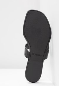 Sandale noire avec une sangle texturée, semelle plate et un design minimaliste. Présente le logo Calvin Klein sur la semelle intérieure.