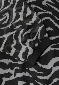 Tessuto stampato animale in bianco e nero con dettagli a polsino nero a coste; materiale leggero e testurizzato con un design fluido.