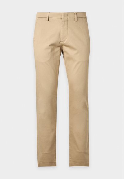 Beige slim-fit bukser med bæltestropper og forlommer, vist mod en ensfarvet hvid baggrund.