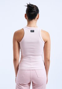 Top in cotone a coste di un rosa chiaro, con scollatura rotonda e design a racerback. Presenta un piccolo etichetta del marchio vicino all'area della spalla.