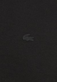 Zwart katoen met een ribbelstructuur, gekenmerkt door een klein, reliëf zwart krokodillenlogo aan de linkerkant.