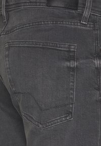 Jeans de denim negro con un bolsillo trasero con costura curva, textura suave y un brillo sutil, etiquetados con el nombre de la marca Esprit.