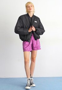 Zwarte pufferjack, roze luipaardprint shorts en zwarte high-top sneakers. Gladde stof, oversized ontwerp en opvallende patronen op de shorts.