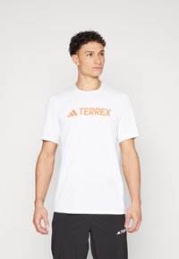 Valge lühikeste varrukatega T-särki, mis on valmistatud kerge materjali hulgast, kujundusega, millel on oranž "TERREX" logo rinna kohal. Lihtne, puhas disain.