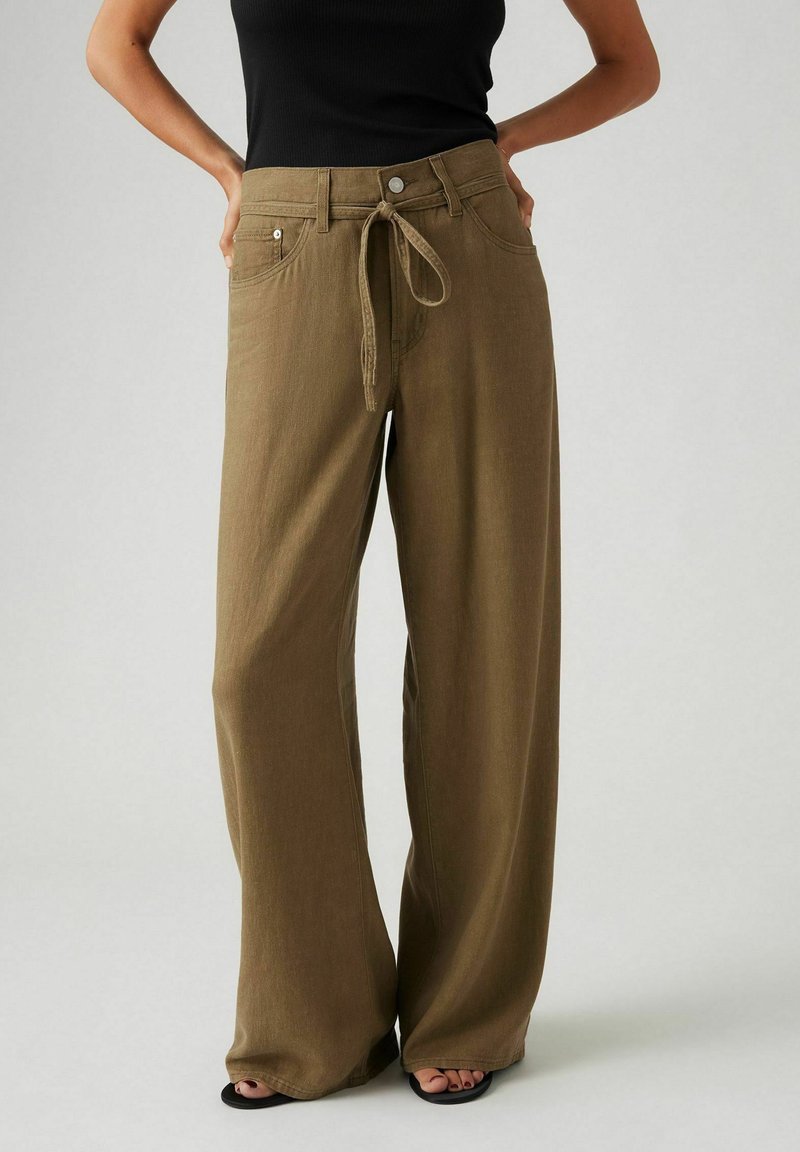 Pantalons large en tissu vert olive doux, avec une taille à cordon, des poches avant et une coupe décontractée pour le confort.