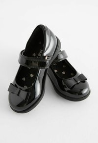 Schwarze Lackleder-Mary-Jane-Schuhe mit einem Riemen, runder Spitze und einer dekorativen Schleife an der Vorderseite. Das Innere zeigt ein Herzmuster.
