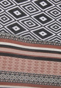 Gemusterter Stoff mit geometrischen Designs in Schwarz und Weiß, ergänzt durch Streifen in erdigen Tönen und komplexen, spitzenähnlichen Details.