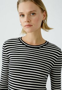 Pull rayé noir et blanc à côtes avec un col rond, des manches longues et un tissu texturé. Présente un design ajusté.