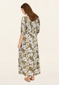 Maxikleid in Olivgrün mit floralem Muster in Hellblau und Creme. Mit kurzen, puffartigen Ärmeln und elastischem Bund, getragen mit flachen, geflochtenen Schuhen.