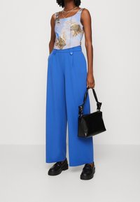 Ljusblå tanktop med tryckt mönster, vida blå byxor med dubbla knappar, svart strukturerad handväska och svarta plattformsskor.