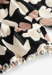 Tessuto a coste con motivi floreali astratti neri, beige e marroni e bordi arricciati su sfondo bianco.