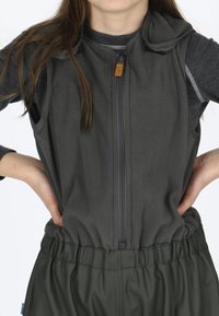 Grå fleecevest med frontlynlås, justerbar krave og elastisk talje, båret over en langærmet mørk beklædning i en neutral indstilling.