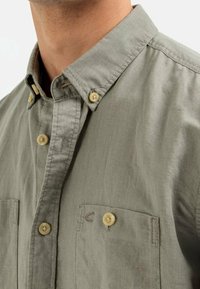 Kortebroek met kraag in gedempte groene stof. Heeft twee voorzakken en een lichtgewicht textuur met beige knopen. Klein logo op de borst.