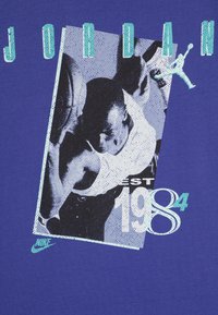 Purple T-shirt featuring a graphic print of a player, 'JORDAN' in bold letters, 'EST 1984', and a Nike logo, all in contrasting colors.