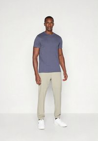 Herrens avslappnade outfit med en figursydd marinblå t-shirt och ljusbeige avsmalnande byxor, kombinerat med vita lågskor.