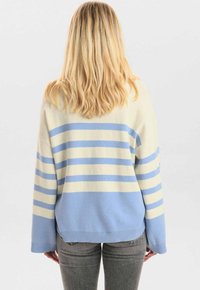 Pull léger en crème et bleu clair avec des rayures horizontales, coupe oversized, épaules tombantes et détails de bord côtelé en bas.