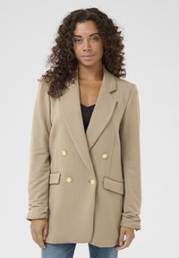 Beige dvouřadý blazer se zlatými knoflíky, klopami a předními kapsami. Hladká tkanina, dlouhé rukávy a přiléhavý střih.