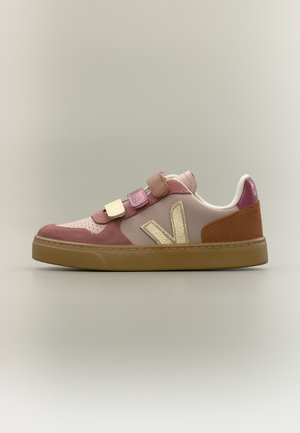 Low-top sneaker met roze, paarse, crèmekleurige en bruine panelen, drie klittenbandriemen, gouden zijlogo en gumrubberen zool op een neutrale achtergrond.