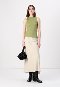 Ljus olivgrön ribbad ärmlös topp, krämfärgad maxikjol, svarta knähöga stövlar och en svart väska med blommiga detaljer.