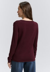 Bordeaux langemouwen trui met een ronde halslijn, geribbelde manchetten en een gladde textuur. Draagt met losse denim broeken.