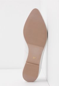 Chaussure blanche montrant sa semelle en caoutchouc beige, qui présente une surface texturée et un design sans talon ; taille marquée 37 en jaune.
