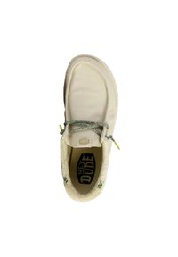 Chaussure slip-on en toile blanche avec un dessus texturé, des coutures contrastantes, des lacets élastiques et une semelle intérieure à motifs portant le nom de la marque "HEY DUDE."
