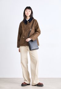 Brown, waterproof jacket with a navy collar, two front pockets; paired with beige wide-leg trousers and brown platform shoes. Black crossbody bag.