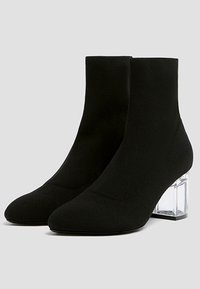 Bottines en tissu noir avec un design extensible, bout pointu et talon bloc transparent, présentant une texture côtelée.