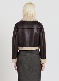 Giacca in finta pelle marrone con colletto e polsini in shearling beige, caratterizzata da un design corto e una texture liscia. Senza hardware visibile.