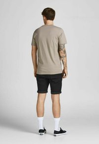 Jasno beżowy T-shirt z krótkim rękawem, czarne szorty z podwiniętymi nogawkami, białe skarpetki i czarne sneakersy; tatuaże widoczne na lewym ramieniu.