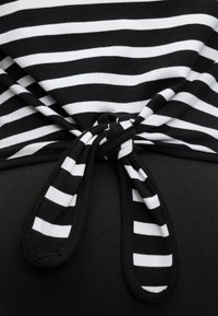 Čierno-biela horizontálne pruhovaná látka zviazaná do uzla na pozadí z pevnej čiernej látky.