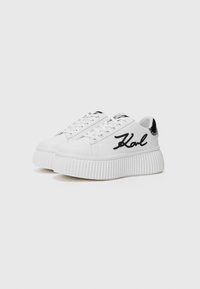 Hvite plattform-sneakers med ribbede såler, snøring foran og svart brodert "Karl"-detalj på siden, med en teksturert overflate.