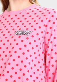 Vaaleanpunainen puuvillaneule, jossa on punaisia pilkkuja ja brodeerattu "CANDY" -tekstilogo. Pyöreä pääntie, pitkät hihat, pehmeä pinta.