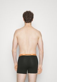 Čierne bavlnené boxerky s oranžovým elastickým pásom označeným "BJÖRN BORG." Model je zobrazený zozadu, na neutrálnom pozadí.