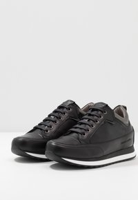 Svarta lädersneakers med grå detaljer, med snörningsdesign, vadderad sula och subtilt varumärkeslogo på sidan. Avslappnad stil.