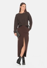 Maglione marrone a coste con bordo in pizzo, abbinato a una gonna marrone aderente con spacco laterale. Stivali alla caviglia neri con tacco e una borsa a tracolla con motivo.