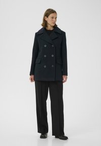 Tamsiai mėlynas dvigubai užsegamas peacoat'as su dideliais mygtukais, iškirpte su sąsagėlėmis ir priekinių kišenių, derinamas su juodomis plačiomis kelnėmis.