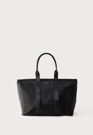 Grande borsa a mano nera con due tracolle, forma rettangolare e etichetta del marchio discreta sulla parte anteriore, su sfondo bianco uniforme.